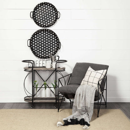 Black Solid Wood and Steel Rolling Kitchen Cart With Storage placed beside a stylish gray chair, featuring round polka-dot trays.
