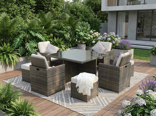 HOMEROOTS Nine Piece Clear and Gray Glass Dining Set on a patio surrounded by greenery and flowers.