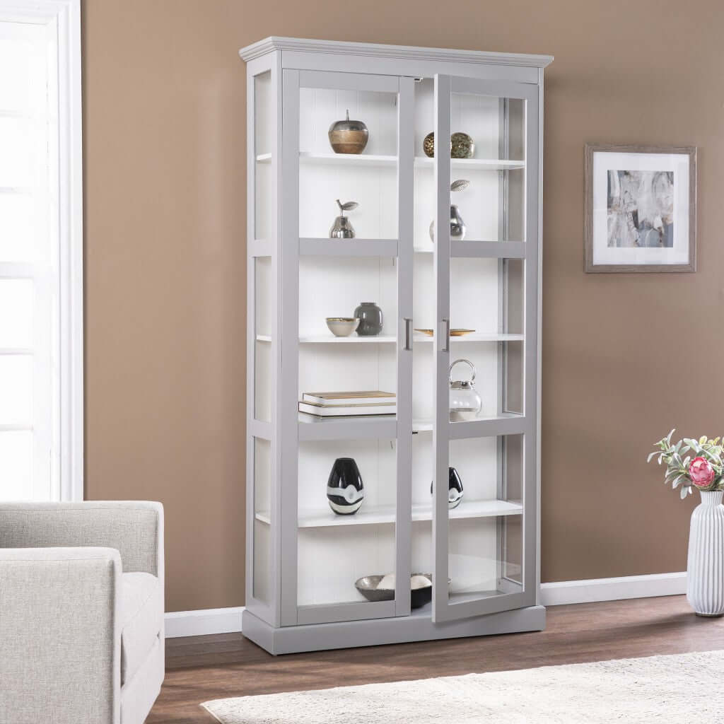 Gray double door curio cabinet with glass shelves showcasing decorative items in a modern living room.